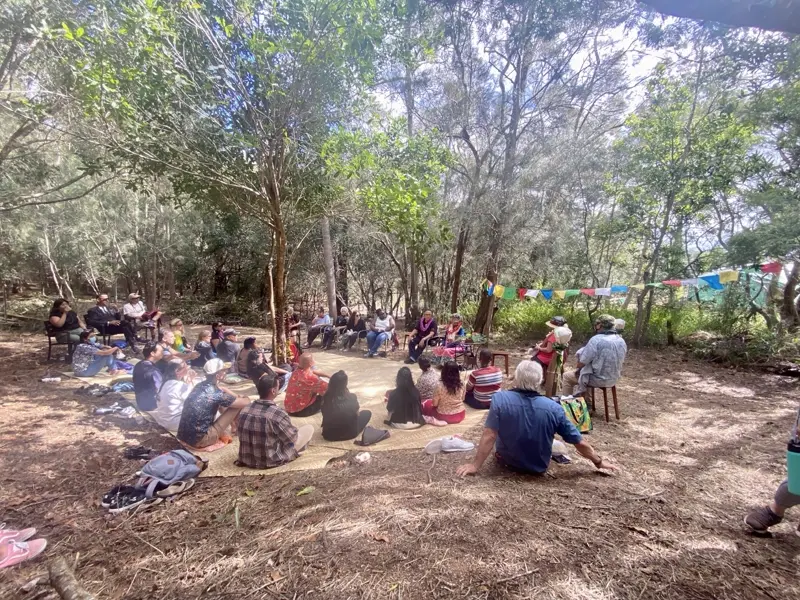 Community members seated together on the grass at Palehua, with peace flags strung through the trees.